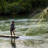 Fischer in einem schmalen Boot wirft ein großes Netz in den Mekong