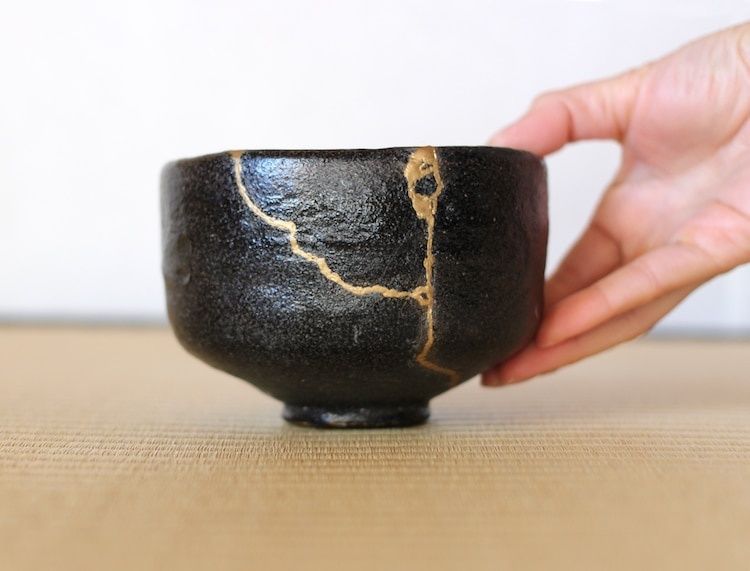 Schwarze Keramikschale mit goldfarbenen Kintsugi-Rissen in einer Hand