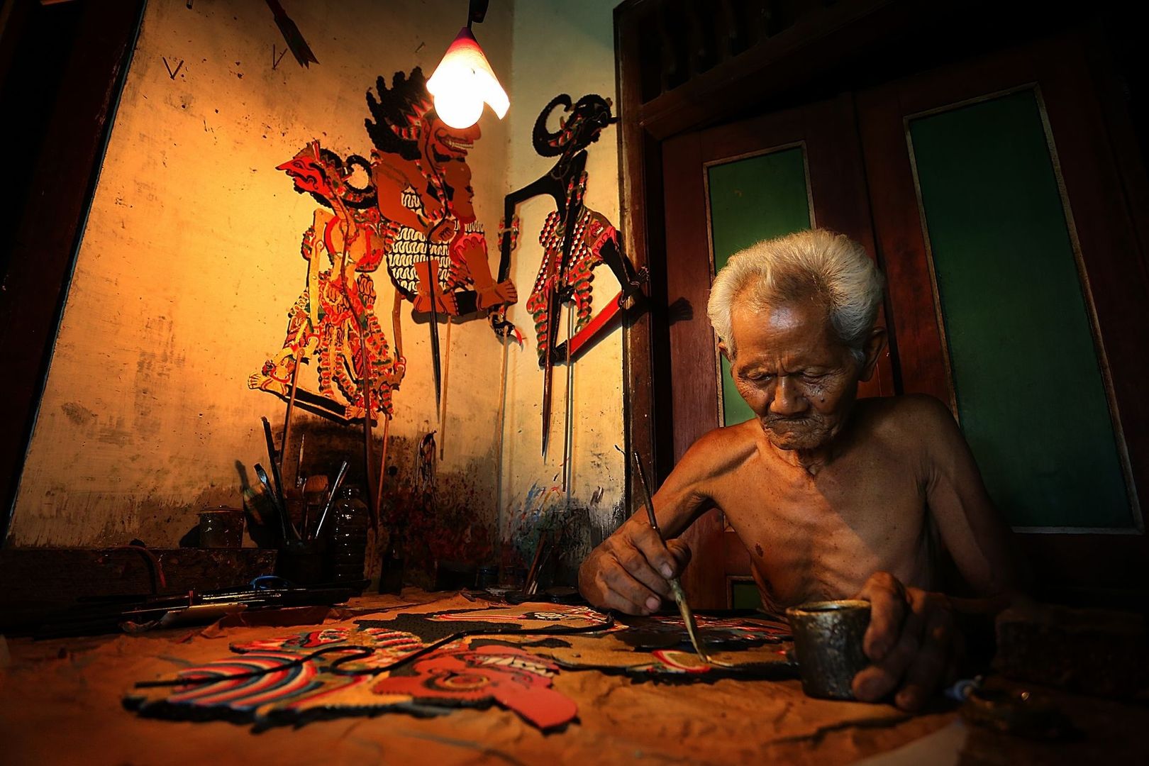 Älterer Mann bemalt Wayang-Kulit-Figuren in einer Werkstatt